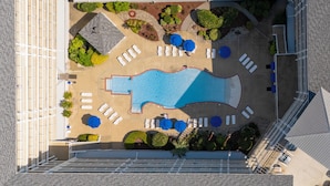 Vista aérea de uma área de piscina de hotel com espreguiçadeiras, piscina e canteiros de jardim ajardinados.