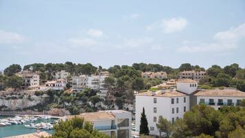 A coastal town with white buildings, a marina, and a cliff with trees.