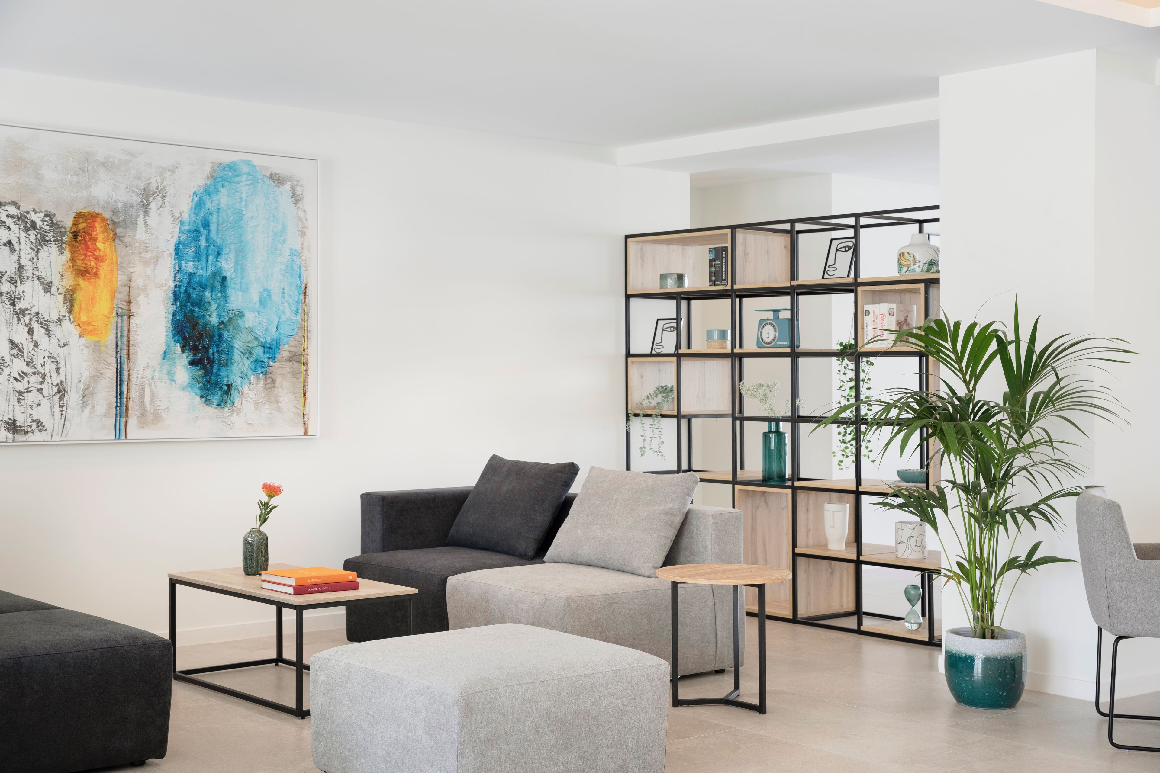 Una sala de estar moderna con un sofá gris, una mesa de centro, una estantería y una planta en maceta.