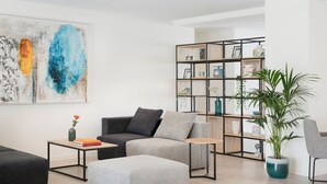 A modern living room with a grey sofa, a coffee table, a bookshelf, and a potted plant. - Marina Drach (Manacor)