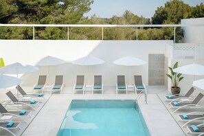 Área da piscina com espreguiçadeiras e guarda-sóis, piscina e vista para árvores.