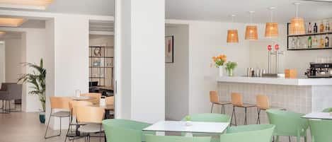 Um café moderno com cadeiras verdes, um espaço de bar com garrafas e uma estante de livros.