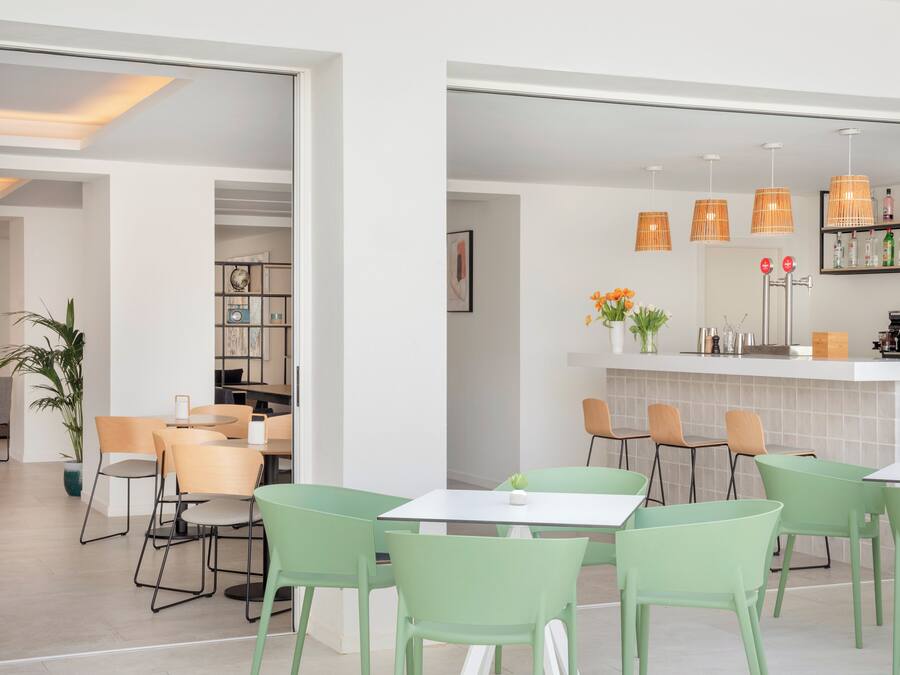 Een moderne café met groene stoelen, een bar met flessen en een boekenplank.