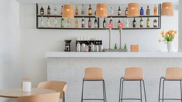 Una zona de bar con una máquina de café, estantes con botellas de licores y tres taburetes de bar.