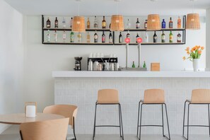 A bar area with a coffee machine, shelves of liquor bottles, and three bar stools. - Marina Drach (Manacor)