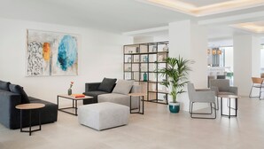 A modern living room with a sectional sofa, ottoman, coffee table, and a bookshelf. - Marina Drach (Manacor)