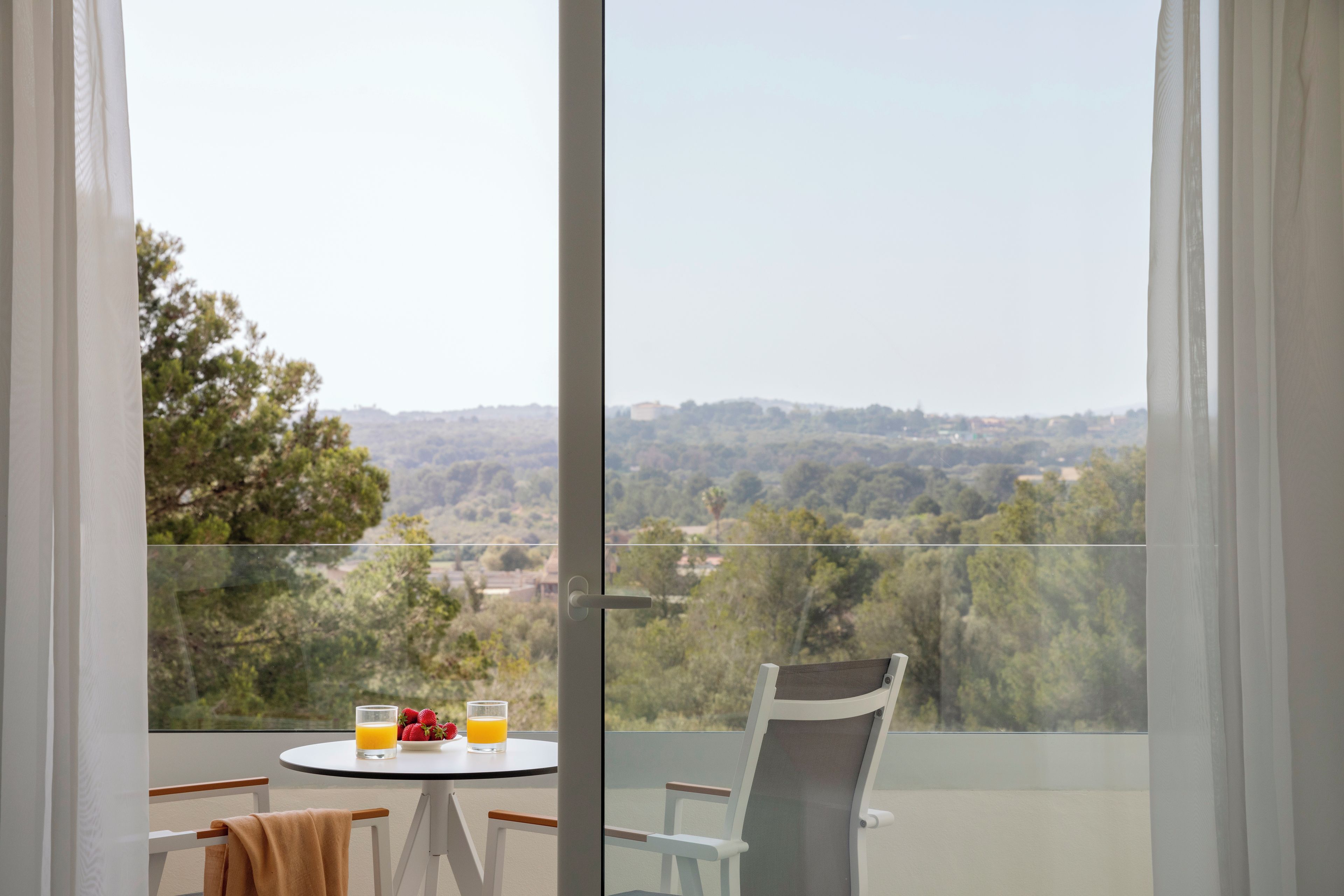 A balcony with a table and chairs, a glass of orange juice, and a bowl of strawberries.