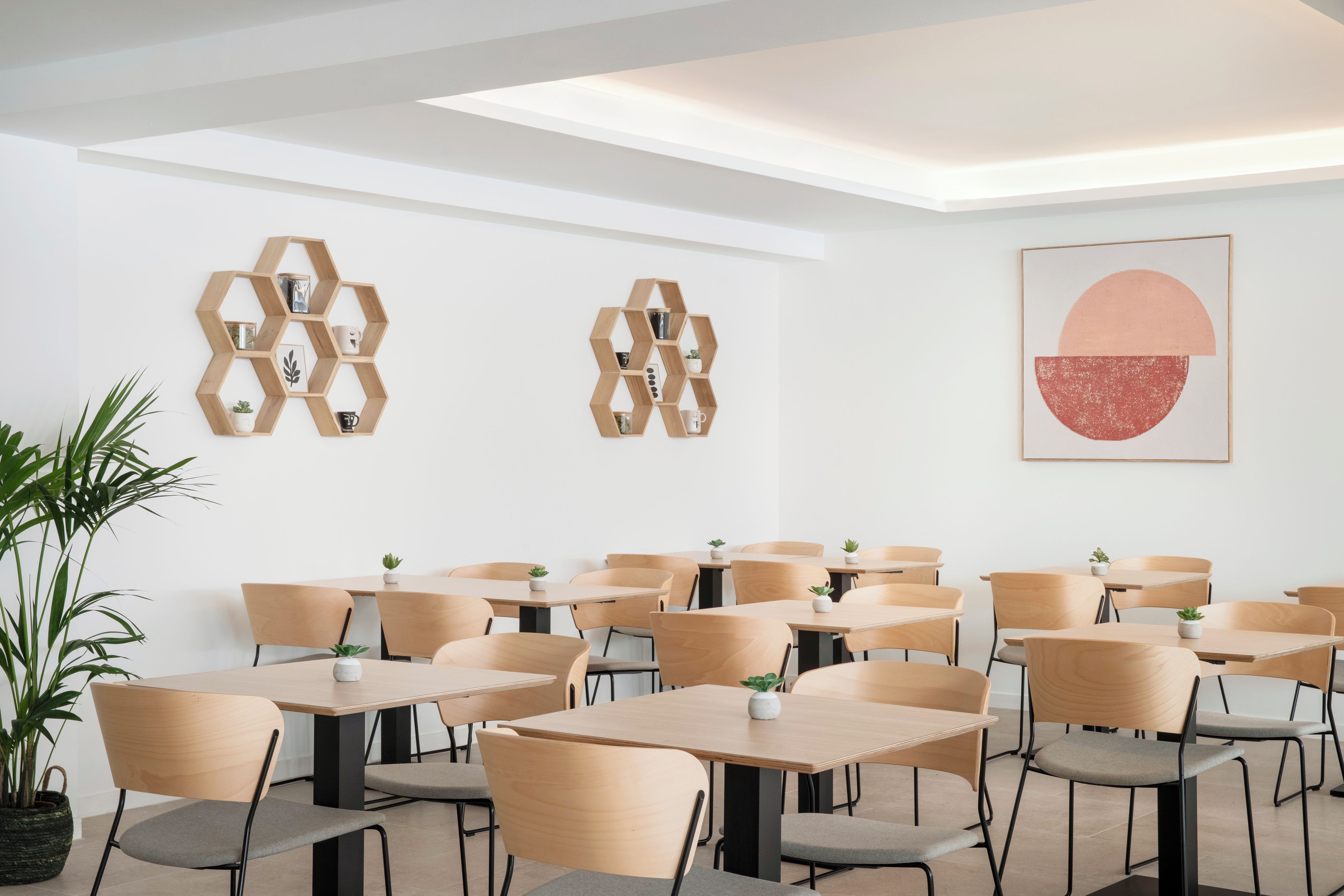 Un espace de salle à manger moderne, doté d’étagères hexagonales en bois, de tables et de chaises au design minimaliste.