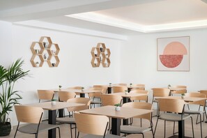 A modern dining area with hexagonal wooden shelves, minimalist tables, and chairs. - Marina Drach (Manacor)