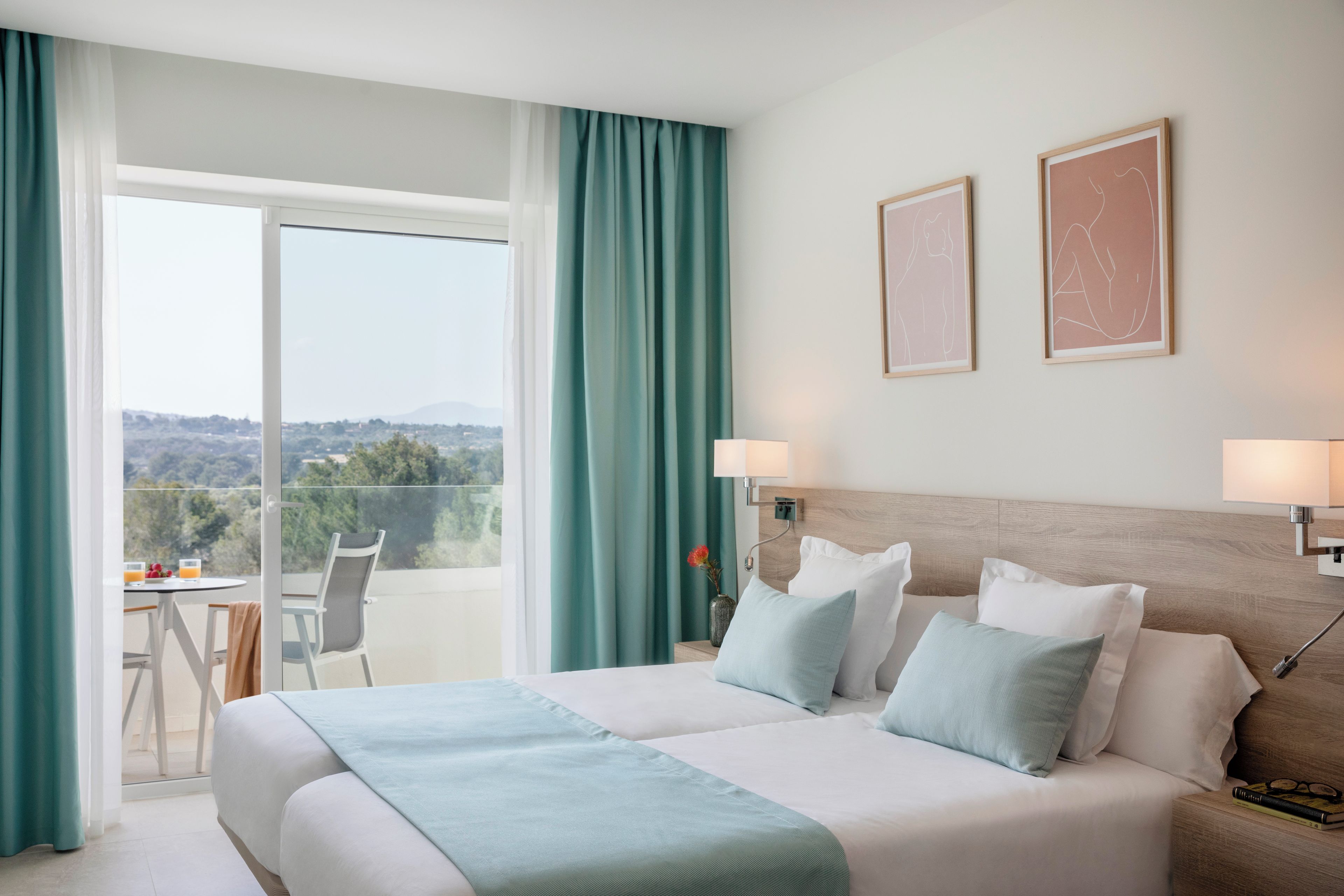 Habitación de hotel con una cama grande, dos lámparas de noche, vistas al exterior y una pequeña mesa con sillas.