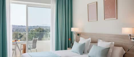 Hotellihuone, jossa on suuri sänky, kaksi yöpöytävalaisinta, näkymä ulos ja pieni pöytä tuoleineen.