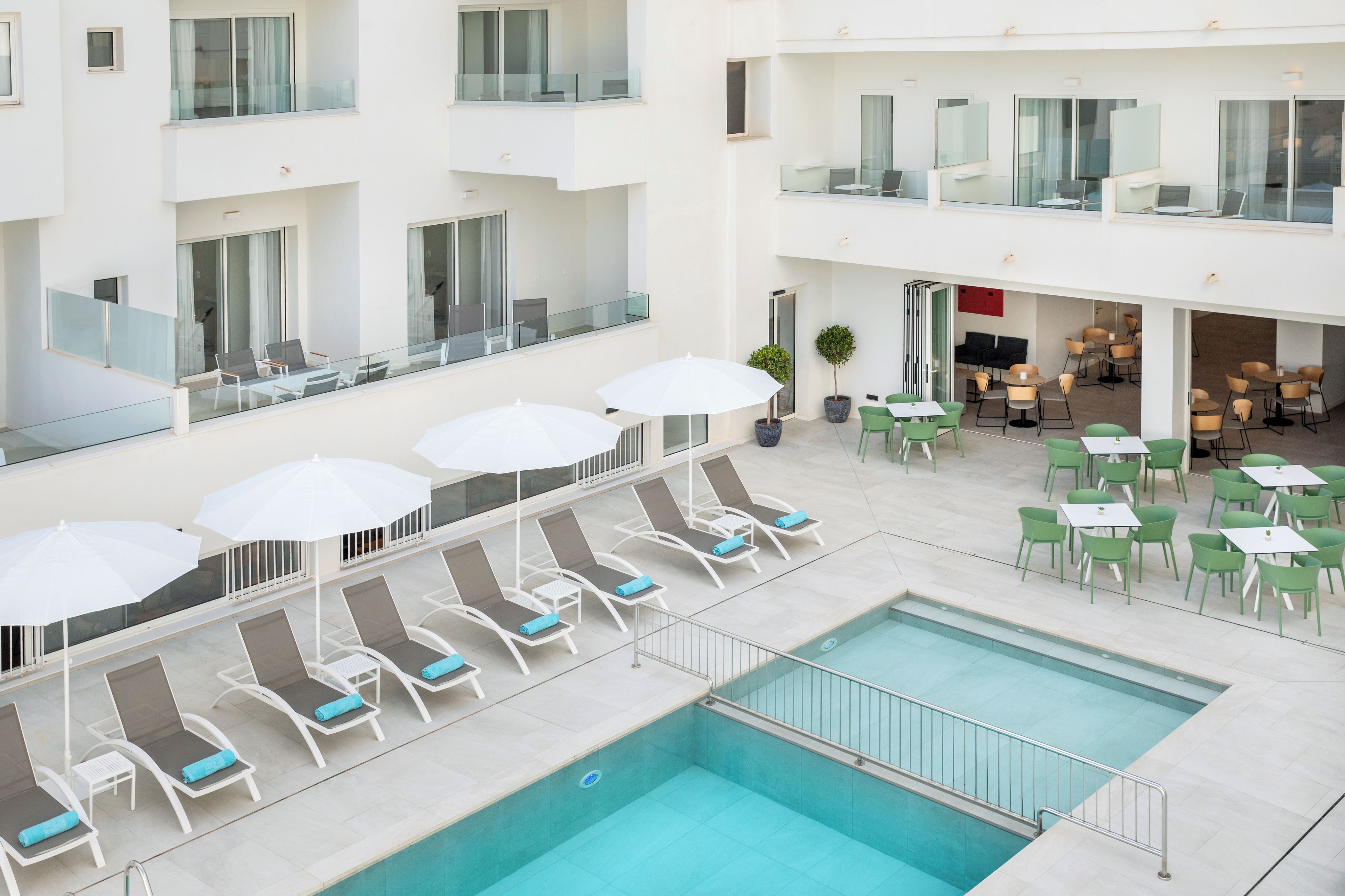 A hotel with a rooftop pool area, lounge chairs, and outdoor dining tables.