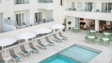 Zona de piscina hotelera con tumbonas, sombrillas y un área de comedor con mesas y sillas.