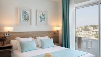 Een hotelkamer met een groot bed, twee kunstwerken in lijsten aan de muur, een balkon met uitzicht en een hoed op het bed.