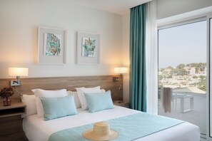 A hotel room with a large bed, two framed artworks on the wall, a balcony with a view, and a hat on the bed. - Marina Drach (Manacor)