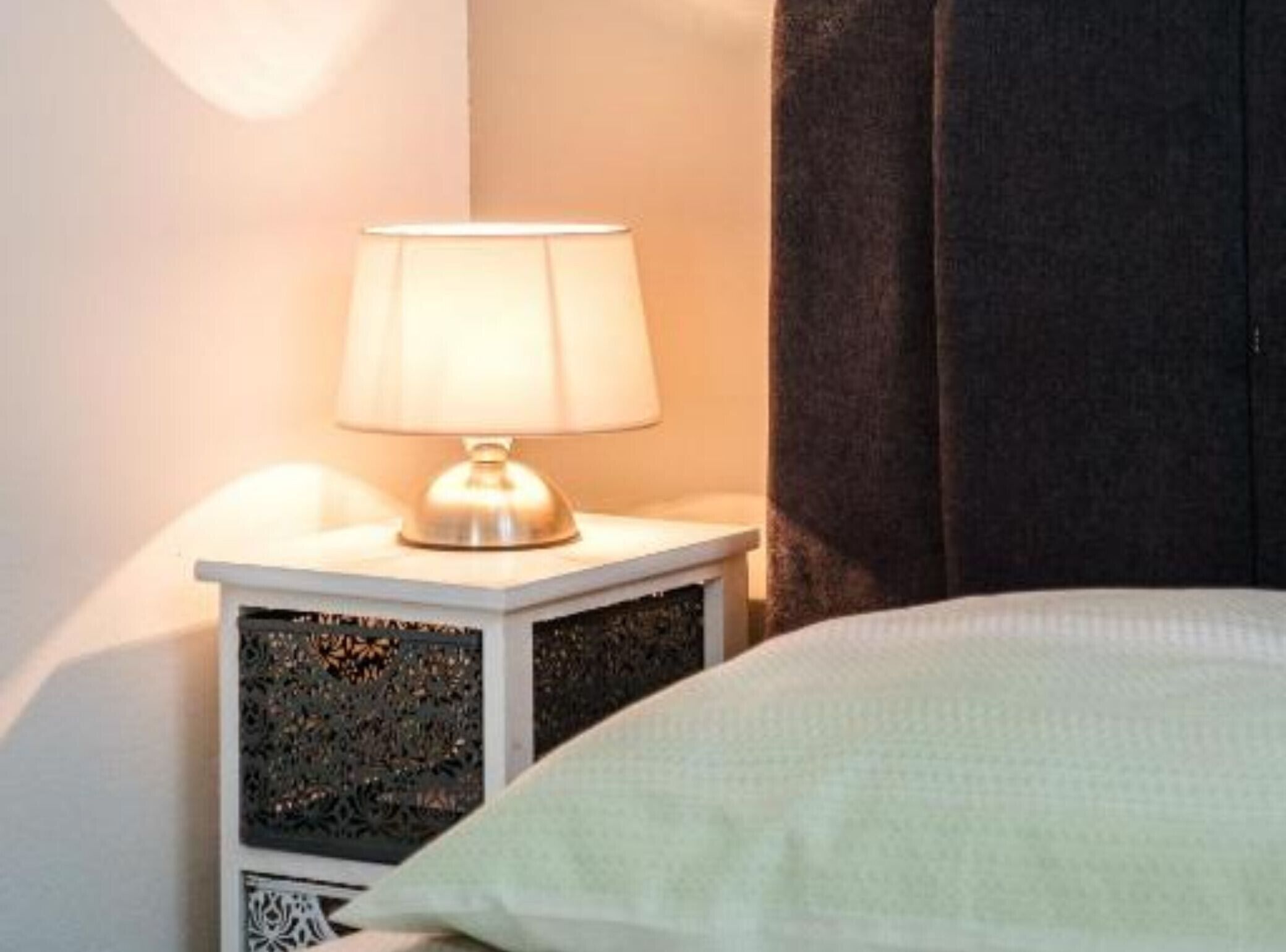 A bed with a white pillow and a nightstand with a lamp.