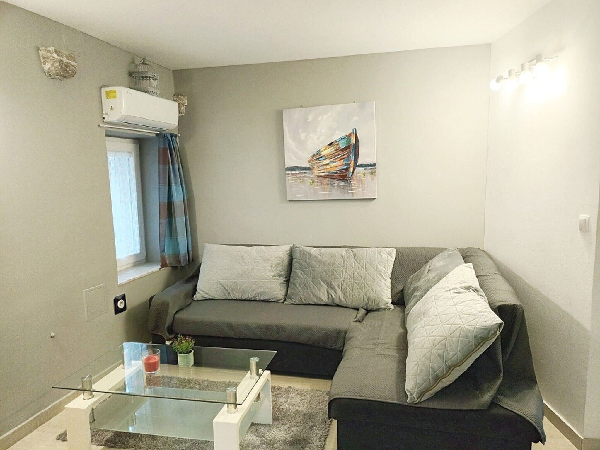 A modern living room with a grey sofa, a glass coffee table, and a painting on the wall.