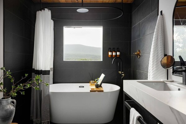 Une salle de bain moderne avec une baignoire sur pieds, une grande fenêtre et un meuble-lavabo avec un miroir.