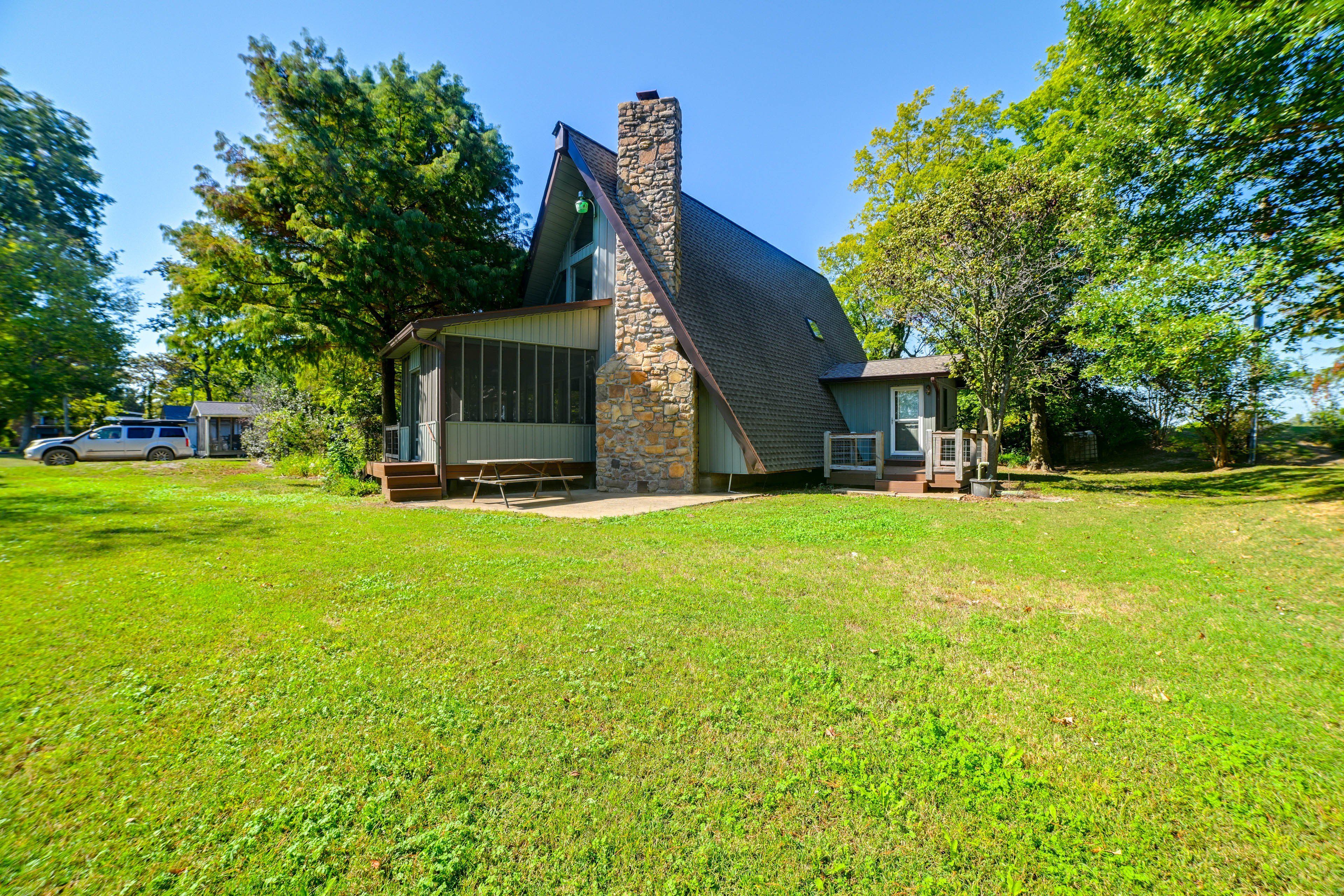 A house with a stone chimney, a large window, and a picnic table in front.
