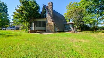 A house with a stone chimney, a large window, and a picnic table in front.