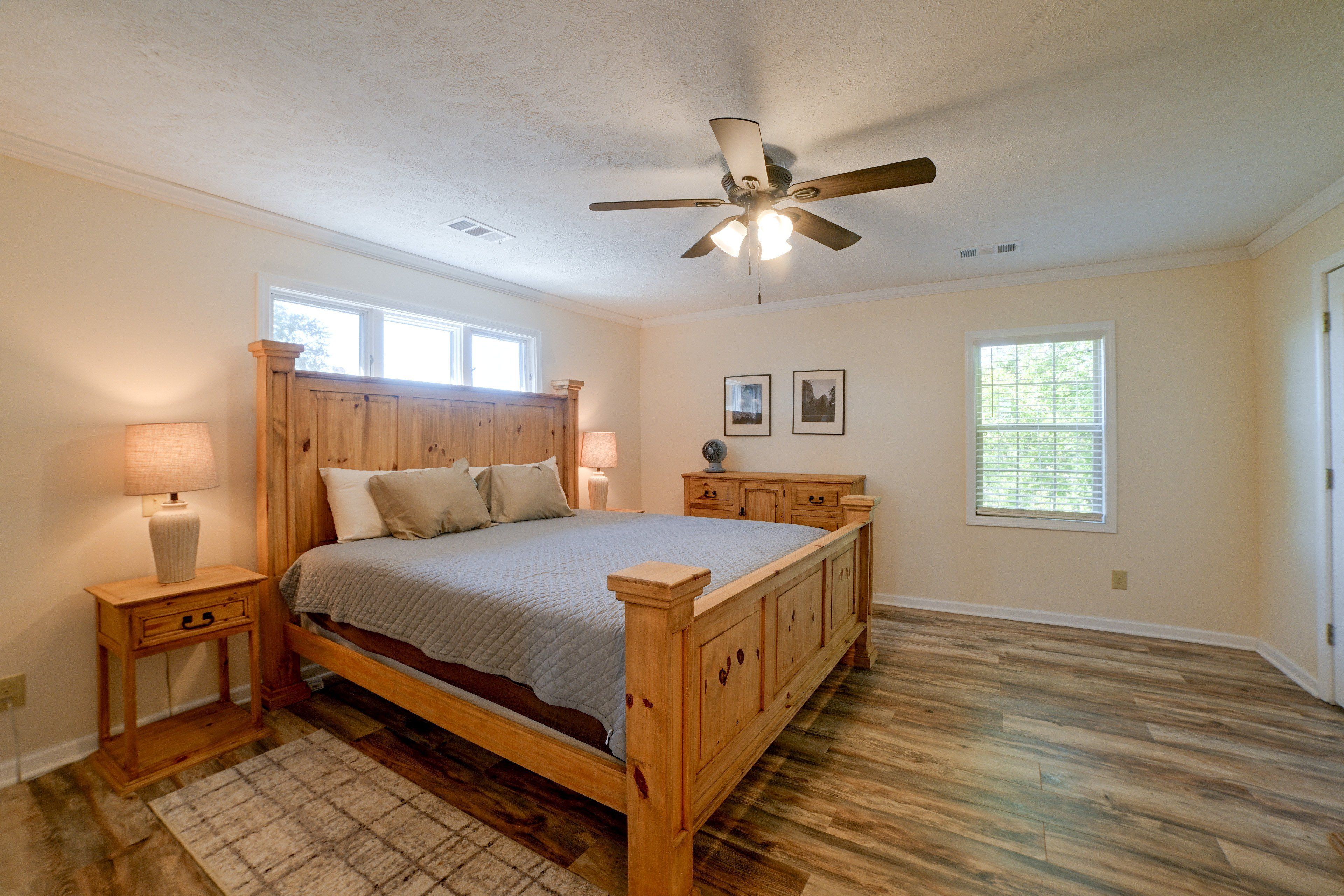 A bedroom with a wooden bed, two bedside tables, a ceiling fan, and two windows.