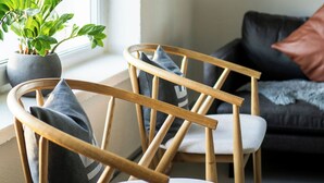 Una sala de estar moderna con una silla de madera, una planta en maceta y un sofá con cojines.
