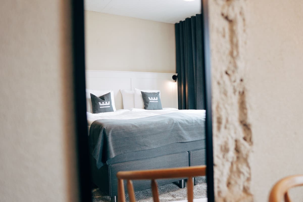 A hotel room with a bed, a chair, and a window with curtains.