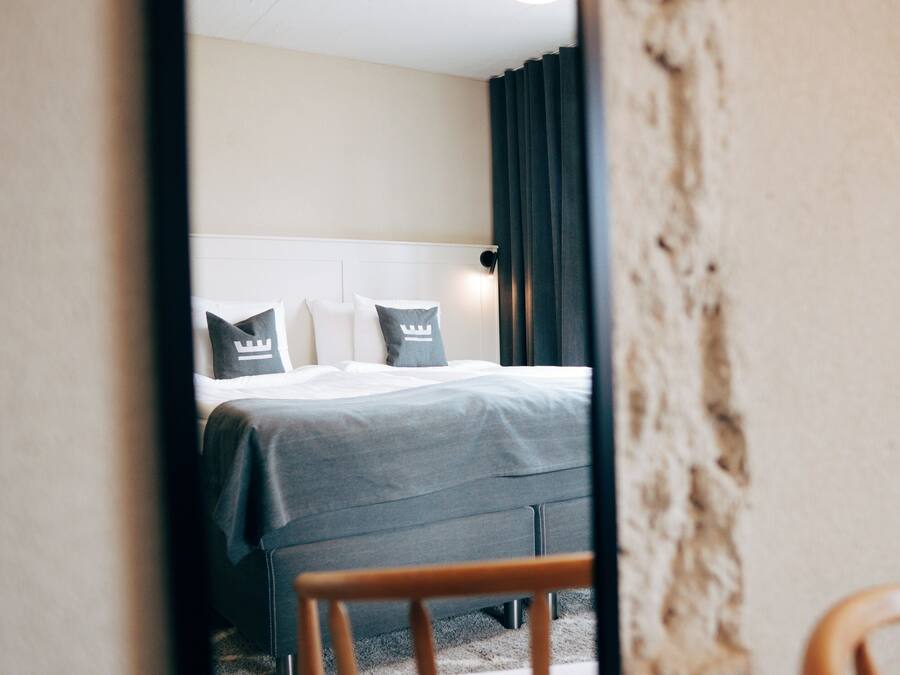 A hotel room with a bed, a chair, and a window with curtains.