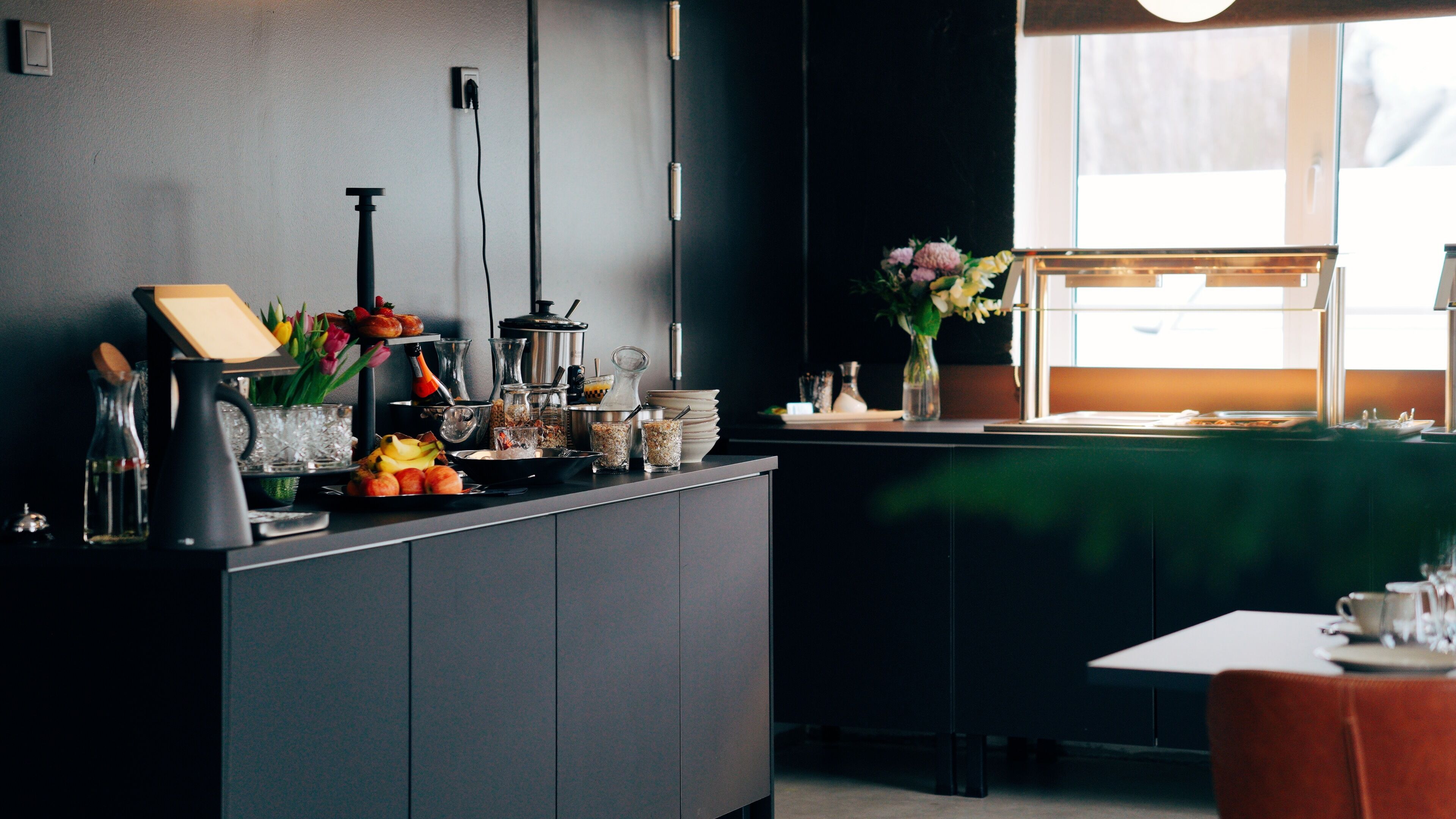 A modern kitchen with a dark countertop, various kitchen appliances, and a window with a view of the outdoors.