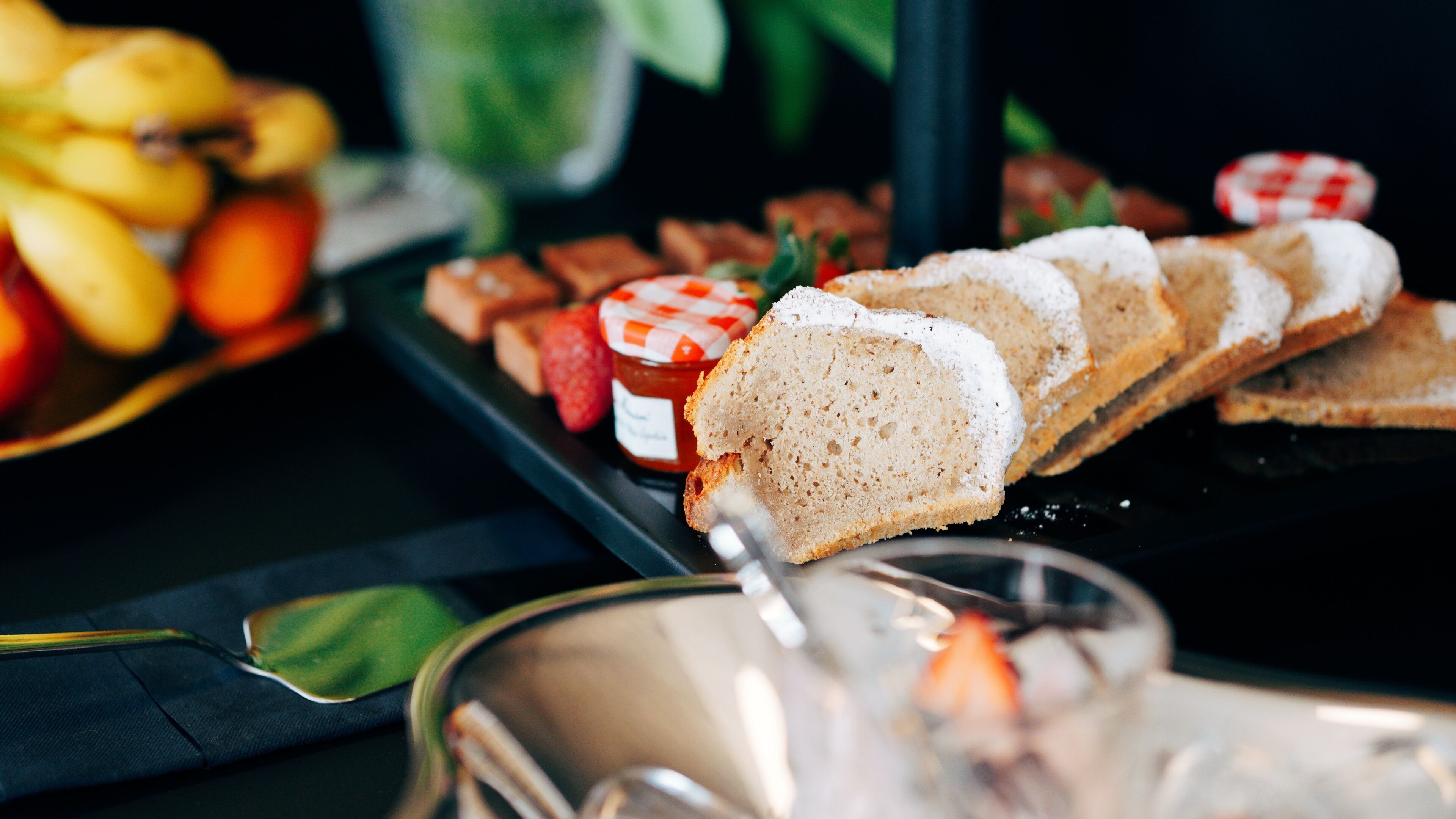 A buffet table with various food items including bread, fruits, and a jar of jam.