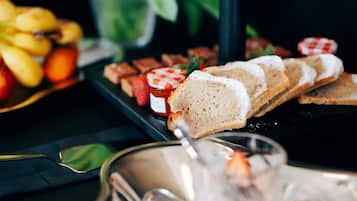 A buffet table with various food items including bread, fruits, and a jar of jam.