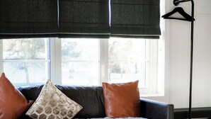 Una sala de estar moderna con un sofá gris oscuro, dos almohadones de cuero marrón, una manta mullida blanca y una mesa de centro de vidrio con objetos decorativos.