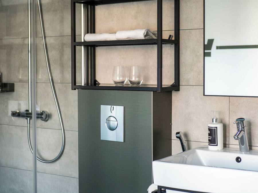Un baño moderno con inodoro, ducha, lavamanos y repisa con toallas y vasos.