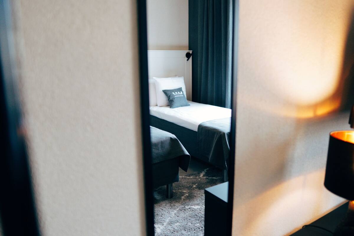 A hotel room with a bed, a bedside table, and a lamp.