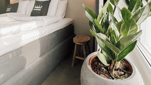 Un dormitorio moderno con una cama, un taburete pequeño y una planta grande en maceta.