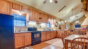 Una cucina con mobili in legno, un frigorifero nero, un forno e una zona pranzo con sedie e tavolo in legno.