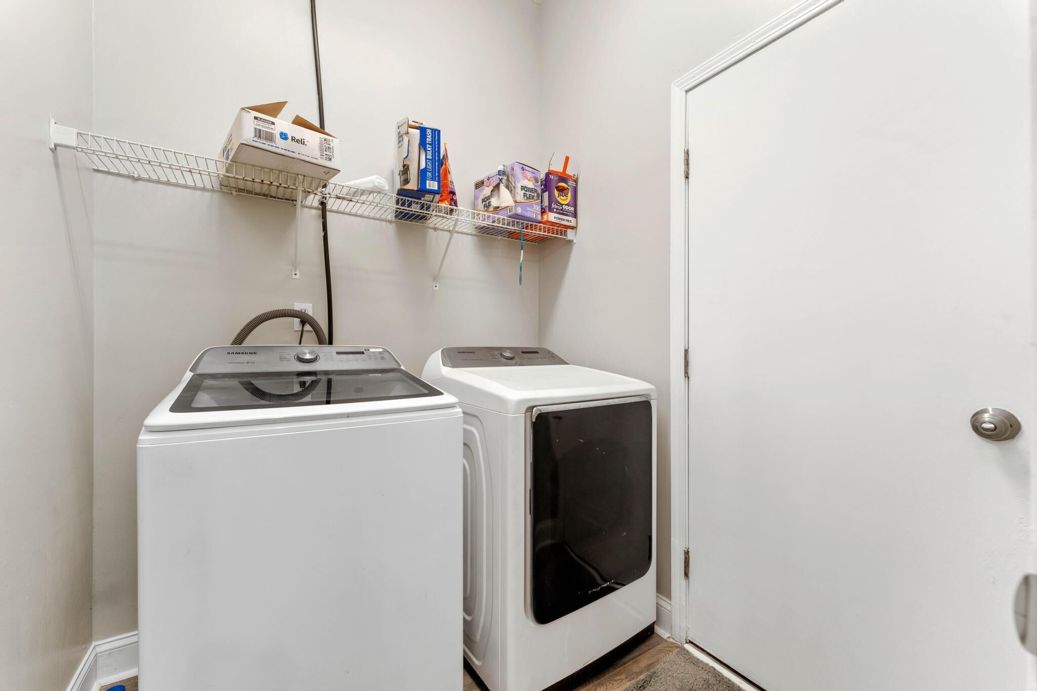 A laundry room with two white washers and dryers, a metal shelf with various boxes, and a door.