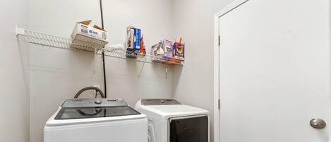 A laundry room with two white washers and dryers, a metal shelf with various boxes, and a door.