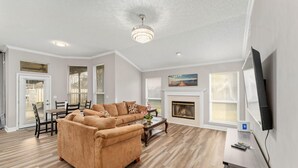 A spacious living room with a beige sofa, a fireplace, and a flat-screen TV mounted on the wall. - Cozy Restful Memory 3BR@Neptune Beach
 (Jacksonville)
