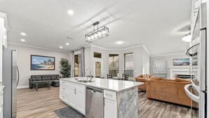 A modern kitchen with a marble island, white cabinetry, and a dining area with a brown sofa. - Cozy Restful Memory 3BR@Neptune Beach
 (Jacksonville)