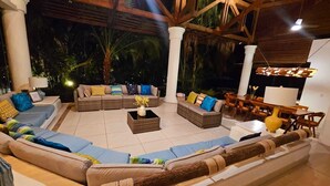 Un espacio al aire libre con sofás y una mesa de centro, rodeado de vigas y columnas de madera, con vistas al exterior.