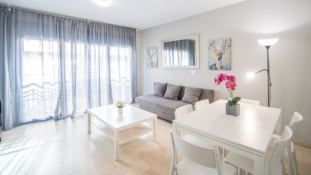 Una sala de estar moderna con un sofá, una mesa de comedor y sillas. Hay cortinas en las ventanas y obras de arte en las paredes.