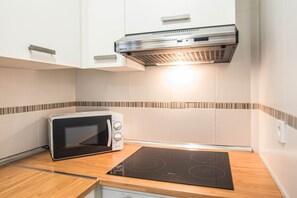 A kitchen with white cabinets, a built-in microwave, and a black induction cooktop. - Céntrico, amplio y confortable (Granada)