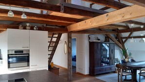 Eine Küche mit Holzbalken, einem eingebauten Ofen und einer Essecke mit Tisch und Stühlen.