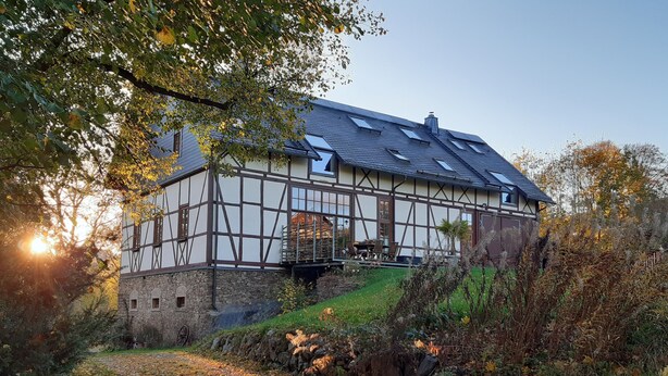 Ein traditionelles Fachwerkhäuschen mit steinernen Fundament, einem Balkon mit Sitzgelegenheit und einem Gartenweg zum Eingang.