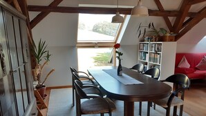 Ein Essbereich mit einem Holztisch, Stühlen, einer Vase mit einer Blume, einem Bücherregal und einem roten Sofa.