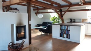 Ein modernes Wohnzimmer mit Kamin, Essbereich, Küche mit eingebautem Bücherregal und großem Fenster für natürliches Licht.