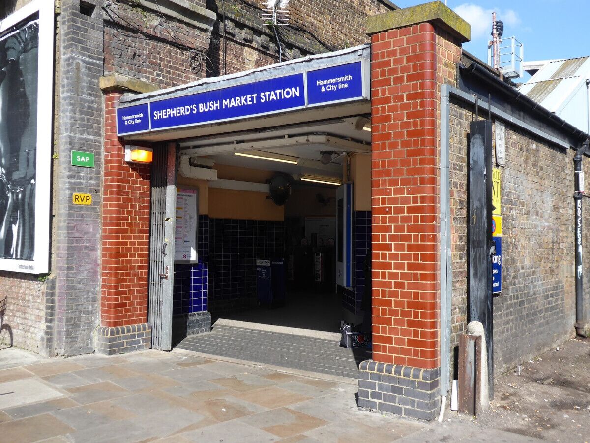 A bus station entrance with a sign reading "Shepherd's Bush Market Station" and "Hammersmith & City Line."