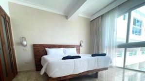 Una cama grande con cabecera de madera en una habitación luminosa con ventanas amplias y vistas al exterior.