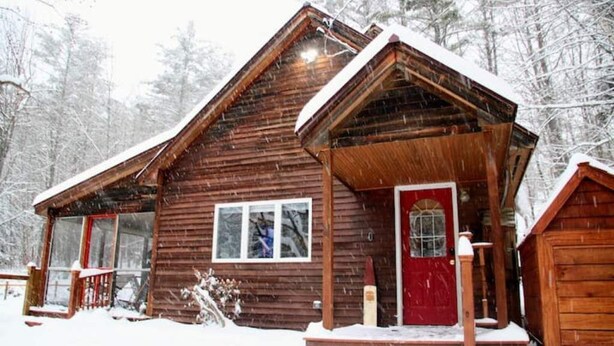 Eine Holzhütte mit roter Tür, umgeben von schneebedeckten Bäumen.